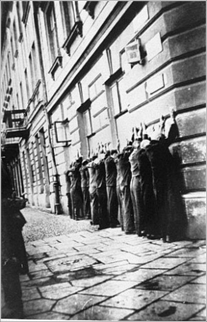 Jews arrested in the Podgorze neighborhood of Krakow are lined up along the pavement with their hands against the wall of a building